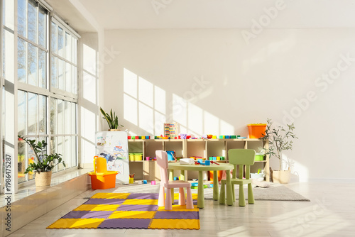 Photos Interior of playroom with table, shelf unit and toys in kindergarten