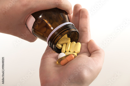 Close-up of hand holding various pills and capsules pouring from brown medicine bottle. Concept of healthcare, medication, treatment, vitamins, and pharmaceutical.