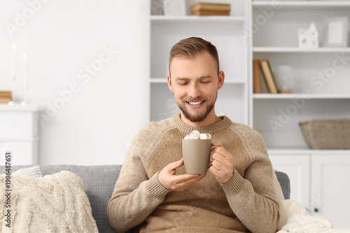 Young man in beige sweater with cocoa sitting on sofa at home