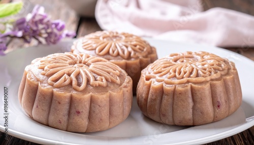 Three ornate sweet red bean paste dumplings with intricate decorative patterns on a white plate, a delightful traditional pastry.