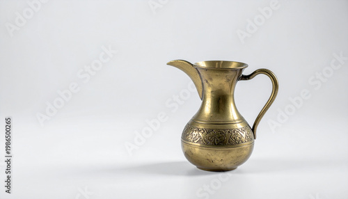 Antique brass pitcher with intricate engraved patterns on a plain white background