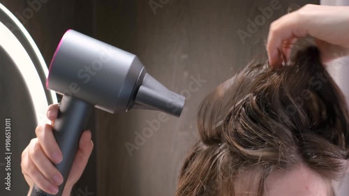 Woman drying her hair with hairdryer on gray background.