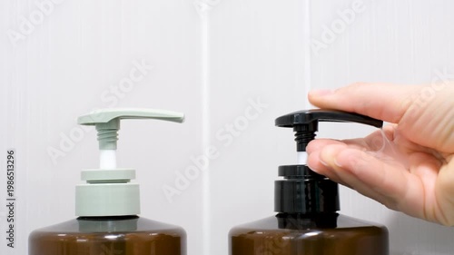 Female hands squeeze shampoo with dispenser close-up against background of gray tiles.