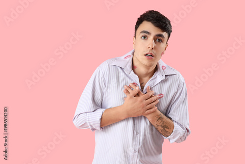 Photos Confused man with kiss marks on his shirt against pink background
