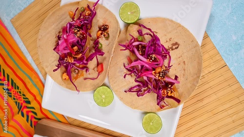 Top view of two battered fish tacos served on corn tortillas on a square white plate. Ensenada-style tacos. Camera rotating from above