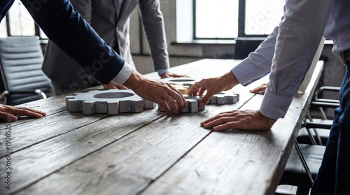 Foto Business team collaboratively assembling large interlocking gear pieces on a rustic wooden table
