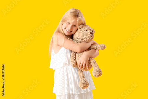 Fotografie Cute little girl with plush teddy bear on yellow background