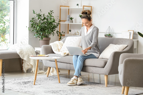 Mature woman with laptop sitting on sofa at home