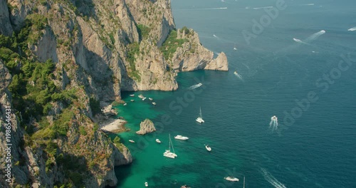 Steep rocky cliffs and turquoise coves filled with boats create a vivid summer scene in Capri Italy
