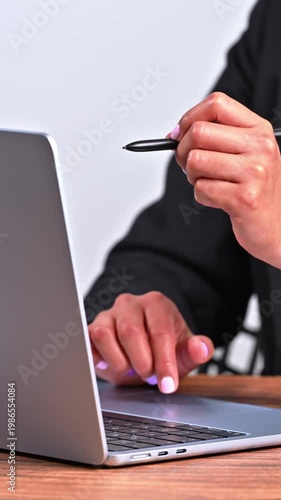 Professional woman in black blazer using a laptop on a wooden desk, multitasking with digital tools