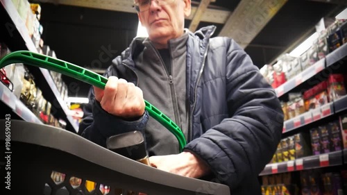 An elderly man examines a jar of instant coffee and puts it into a shopping cart