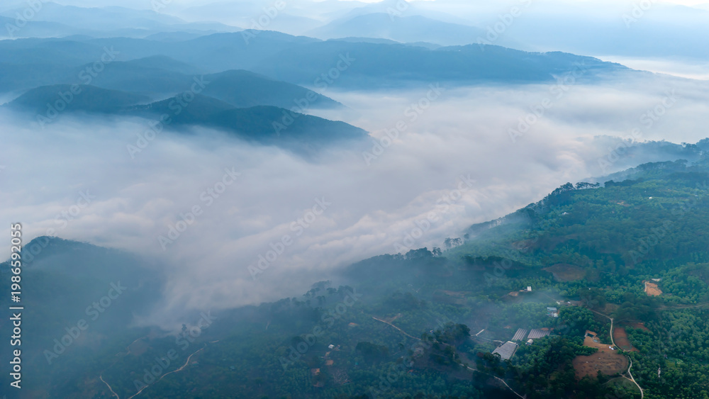 Obraz premium A breathtaking sunrise over layers of misty mountains, where the glowing sun forms a radiant starburst in a golden sky. Soft fog blankets the valleys, creating depth and a dreamy