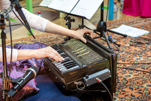 Obraz na plátně Person plays wooden harmonium with shiny keys at cozy kirtan night while singing