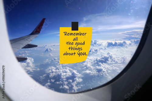 Inspirational motivational quote - Remember all the good things about you. A yellow notepaper sign stick on a flight window, flying high on a blue sky with dramatic clouds background. Self love care.
