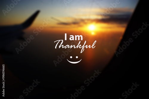 Grateful text on airplane window at sunset - I am grateful with a happy smile sign on a glass. Gratitude concept. Inspirational quote with golden light of the sun on a sunset sunrise sky backgrounds.