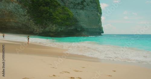 Distant woman enjoying vacations on sandy shore with white foam ocean waves
