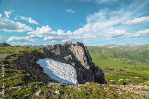 Sunlit grassy meadow, glacier and rocky cliff on precipice edge above alpine ...