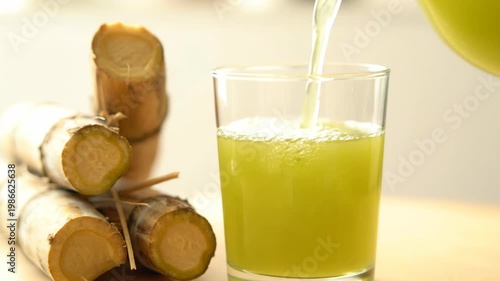 Fresh Sugarcane Juice Pouring into Glass with Cane Stalks