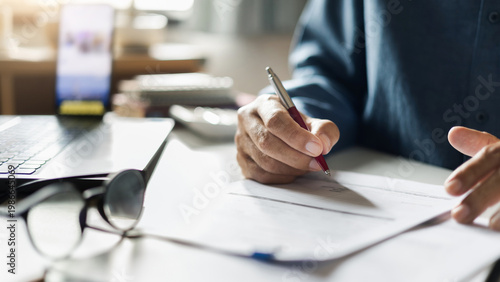 close-up shot, businessman work on desk at home with documents checking business contract, working and meeting online via laptop and mobile phone