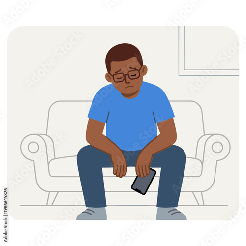 A man sits on a couch looking sad while holding his phone.