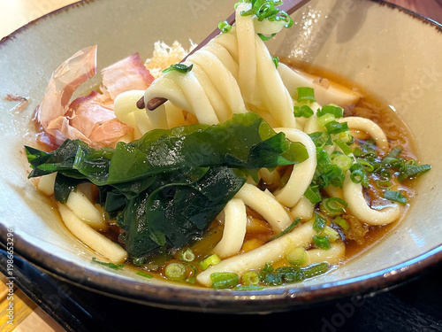 冷たいぶっかけうどん ─ 箸でうどんを持ち上げたアップ・わかめ