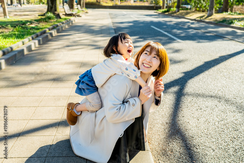 Joyful Japanese Mother and Little Daughter Laughing Together Outdoors in Sunlight