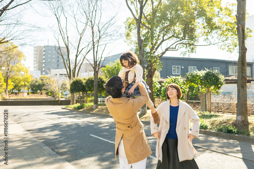 Joyful toddler girl being lifted high in the air by her parents in a winter park, happy family smiling together