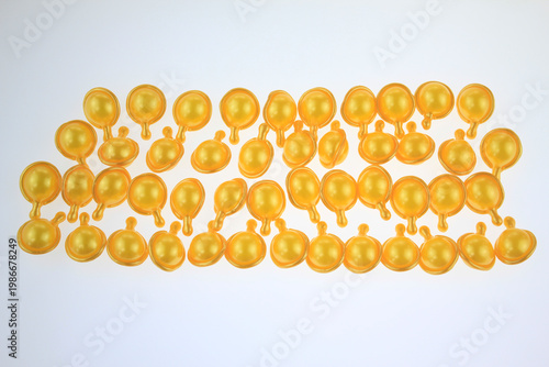 Golden hair serum capsules arranged neatly on a plain white background. Bright, translucent yellow uniform color suggests high quality, products. For self care, hair nutrition, vitamin E hair serum.
