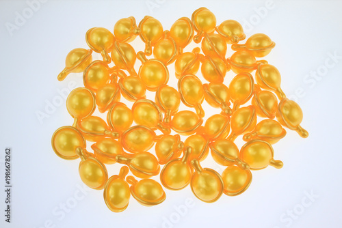 Golden gel  hair serum capsules gleam softly isolated on white background. Each capsule reflects light with smooth, rounded contours.  For hair care routine, hair nutrition, damaged hair repair, serum