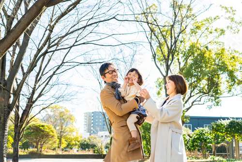 Cute toddler girl winking while being held by her father, parents laughing together in a winter park