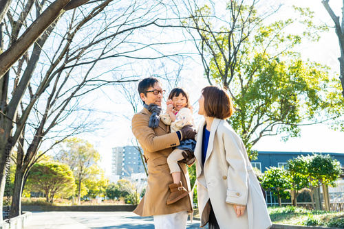 Cute toddler girl winking while being held by her father, parents laughing together in a winter park