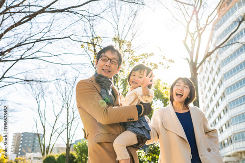 Toddler girl being held by her father and waving at the camera in a winter park, family portrait