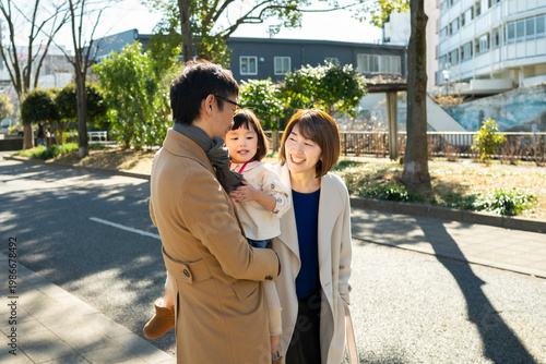 Happy Japanese family walking together on a paved path in an urban park on a sunny winter day, full-length shot