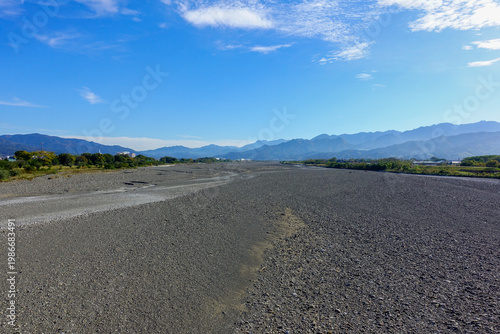 Wide dry riverbed with mountains under blue sky in rural Shikoku landscape