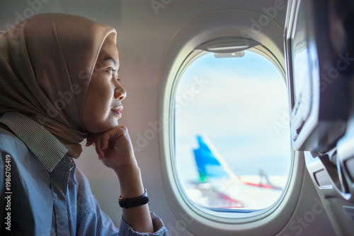 Muslim woman looking through airplane window during flight