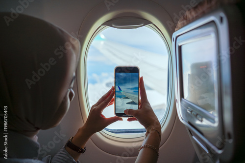 Woman taking photo of airplane wing through window with smartphone