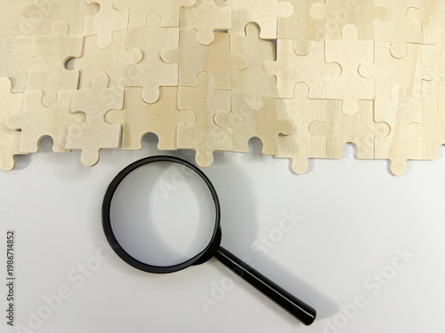Fotografía A black magnifying glass sits below a segment of a wooden jigsaw puzzle, symbolizing searching for missing pieces, detailed analysis, and problem-solving in business strategy