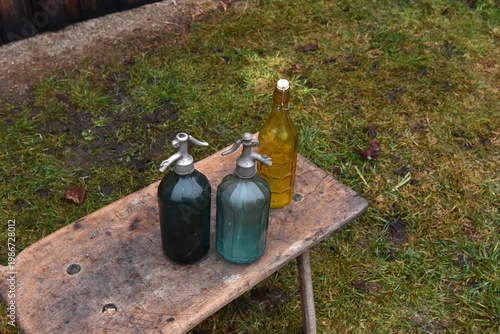 Obraz na plátně Vintage glass soda siphons and yellow bottle on rustic wooden bench