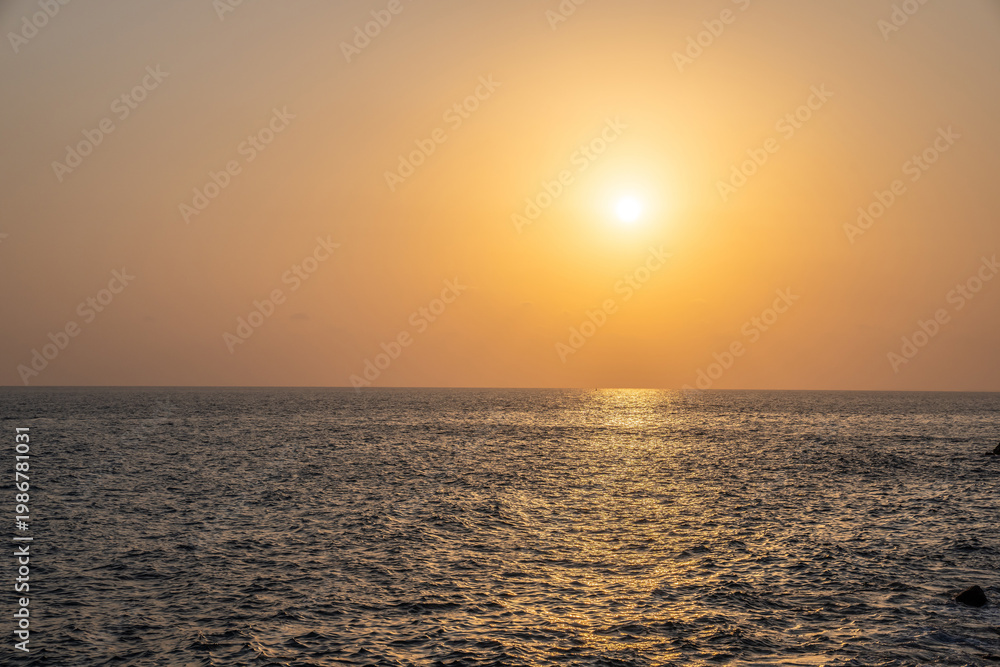 Fototapeta premium Sunset at the sea. The sun is setting in golden haze over the calm sea.