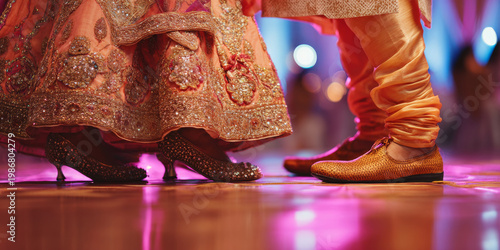 Studio lighting featuring indian wedding dance steps, bride's jeweled sandals beneath richly embroidered lehenga hem beside groom's traditional mojari shoes on polished dance floor, vibrant