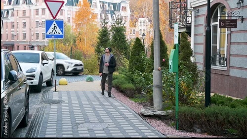 Young Man Walking on a European Cobblestone Street with Coffee Cup in Autumn Cityscape