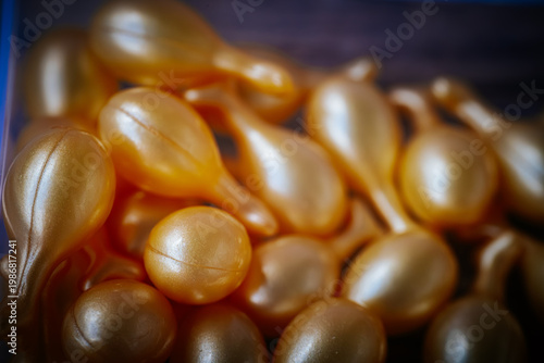 Macro image of several gold serum capsules scattered on a surface, showcasing a shiny texture, even shape, and rich cosmetic appeal with a soft background blur.