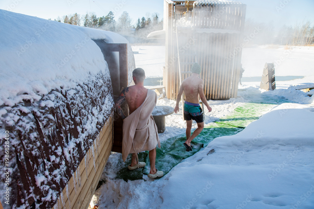 Obraz premium Men exiting outdoor barrel sauna in winter snow, walking to lake ice hole for cold plunge therapy, steam, nordic wellness, sunny day, biohacking