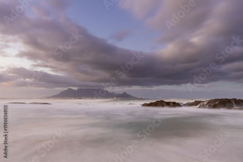 An amazing view from Bloubergstrand beach on the famous table mountain in Cape Town, seen during a colourful sunrise with a amazing dramatic cloudscape and waves braking on the coast from the rough At