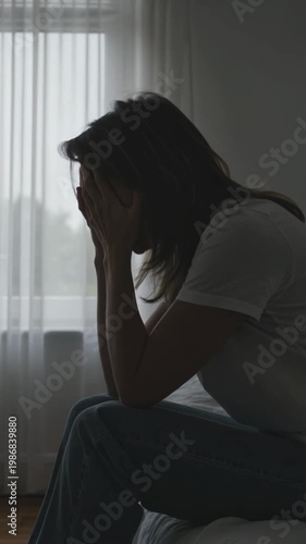 Woman sitting on bed with head in hands in distress, vertical shot