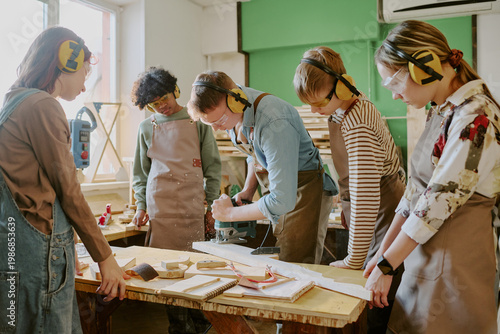Foto Wide shot of diverse teenagers learning woodworking, operating power tool under instructor guidance in workshop