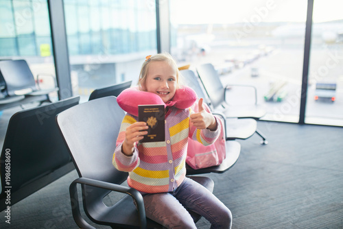 Happy young girl sitting in an airport departure area with a French passport, travel neck pillow and backpack, ready for a family journey or vacation in Europe