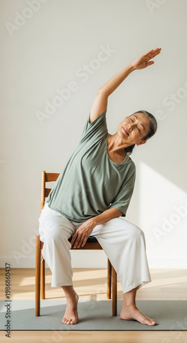 An elderly woman is stretching her arm while sitting on a chair indoors.