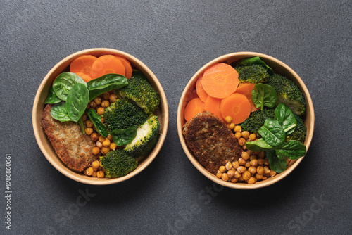 Healthy vegan lunch with broccoli, roasted chickpeas, spinach, carrot and lentil patty in round cardboard container on black background with copy space