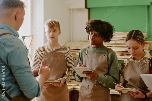 Photography Teenagers attending woodworking class, listening to male instructor and taking notes during practical training
